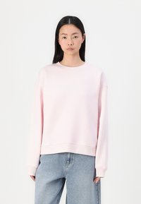Felpa rosa chiaro con scollatura tonda, spalle abbassate e vestibilità rilassata. Realizzata in materiale morbido con polsini e orlo a costine.