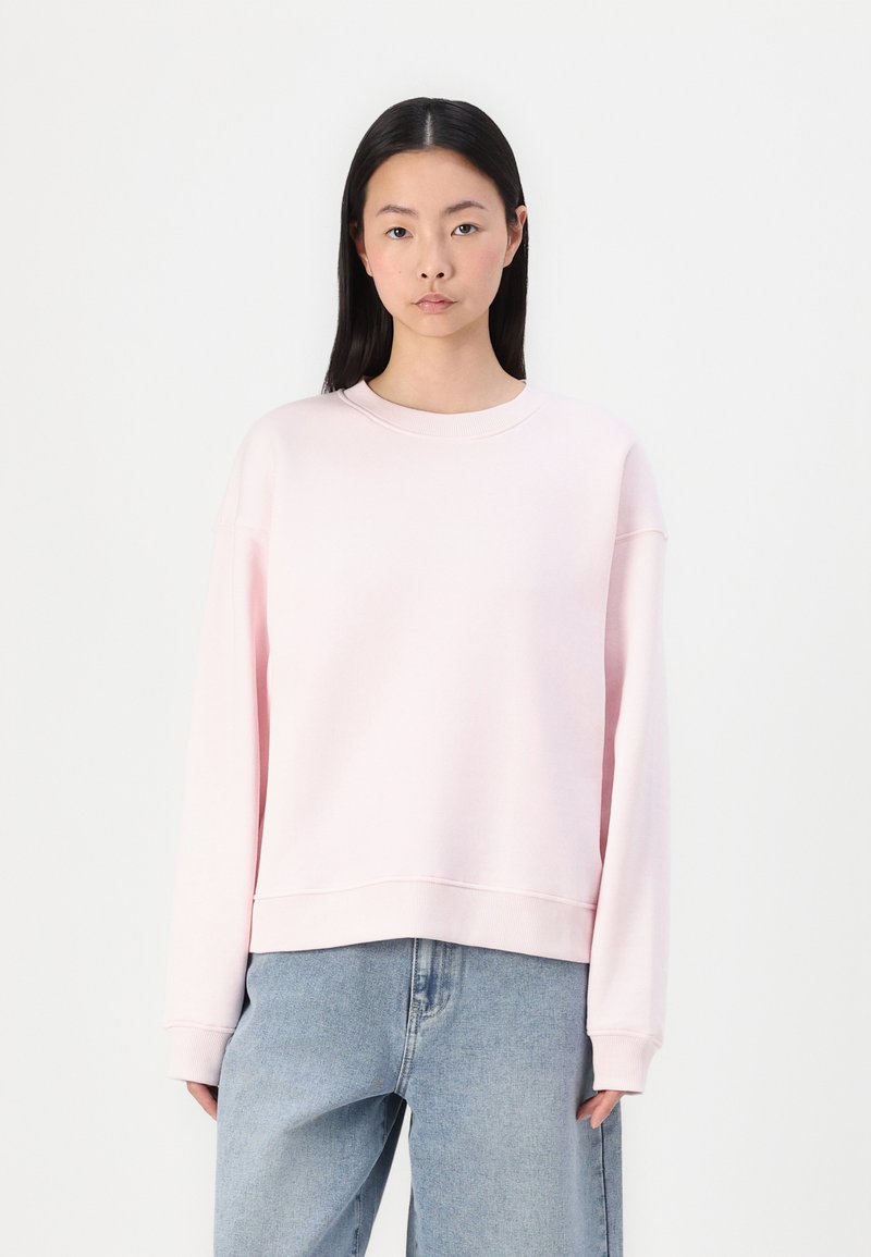 Felpa rosa chiaro con scollatura tonda, spalle abbassate e vestibilità rilassata. Realizzata in materiale morbido con polsini e orlo a costine.