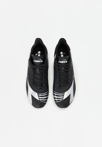 Chaussures de sport noires avec des accents argentés, présentant une tige synthétique lisse, des lacets et une pointe contournée. Détails rayés sur les côtés.