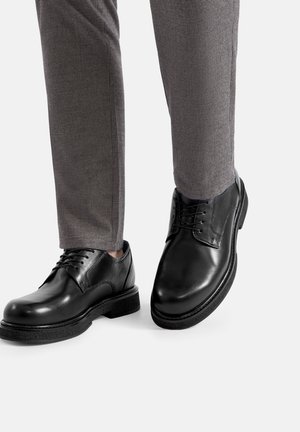 Zapatos de vestir de cuero negro con acabado liso y cordones, combinados con pantalones grises texturizados con un sutil patrón a cuadros.