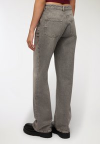 Szare dżinsy z wysokim stanem i prostym krojem, z przetarciami i dwiema tylnymi kieszeniami. Na nogach czarne platformy.