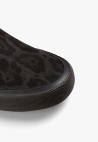 Zapato de ante marrón oscuro con un sutil patrón de leopardo y suela de goma texturizada sobre fondo blanco, mostrando un primer plano del área del dedo del pie.