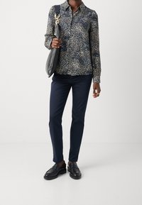 Blusa blu navy con motivo a pois beige chiaro, maniche lunghe, chiusura frontale con bottoni. Abbinata a pantaloni blu navy e mocassini neri. Borsa a tracolla nera.