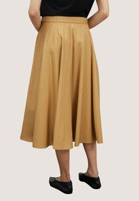 Hnědá, sukně ke kolenům s jemnými sklady a vertikálními proužky; elastický pas, splývavá látka; v kombinaci s černými plochými botami.