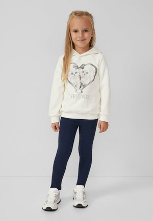 Weißer Hoodie mit einer Herzgrafik von zwei Kätzchen und dem Text "FREUNDE"; kombiniert mit dunkelblauen Leggings und weißen Turnschuhen. Glatte Textur.