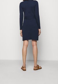 Marinblå långärmad klänning i tröjstil med åtsittande byst, rak silhuett och mjuk textur. Bärs med bruna platta sandaler.