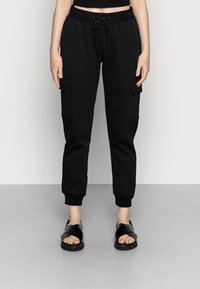 Svarta sweatpants med elastiska mudd, dragsko i midjan och sidofickor i cargo-stil. Bärs med svarta sandaler med remmar.