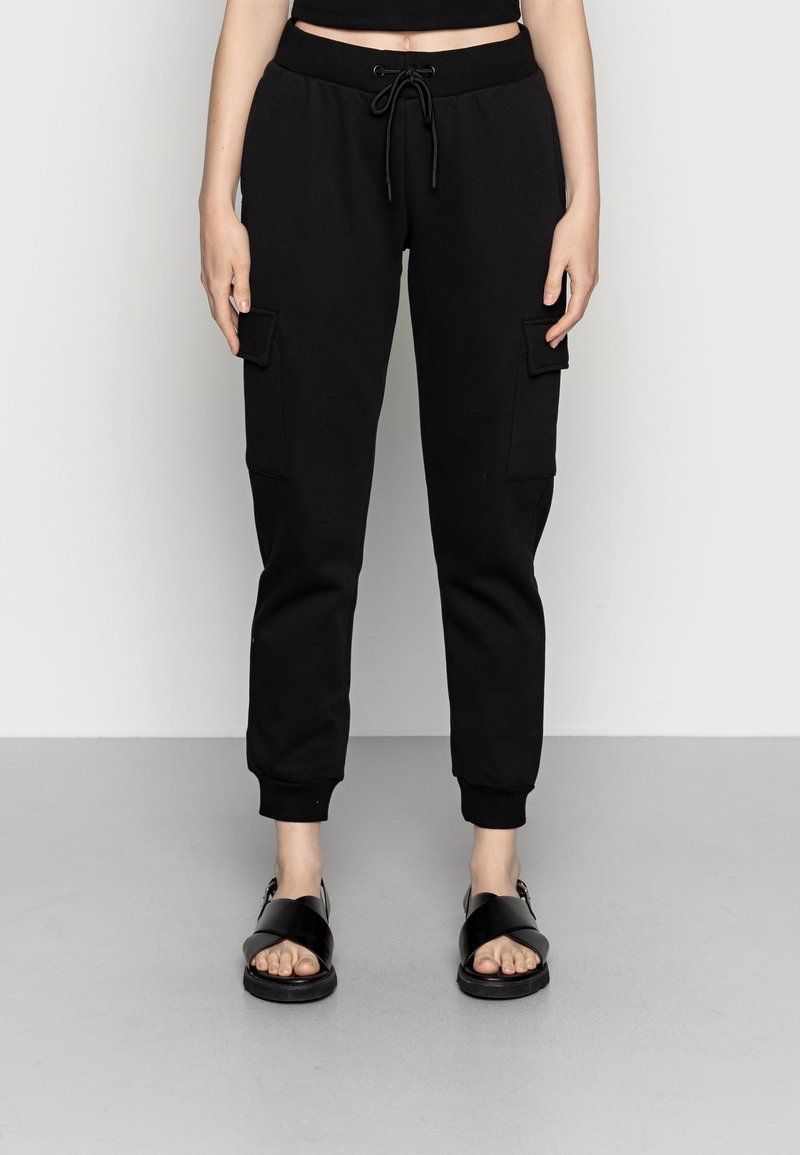 Svarta sweatpants med elastiska mudd, dragsko i midjan och sidofickor i cargo-stil. Bärs med svarta sandaler med remmar.