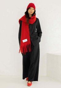 Zwart overhemd met krijtstreep en wijde broek gecombineerd met een felrode wollen sjaal en hoed; rode schoenen met een zachte textuur en eenvoudig ontwerp.