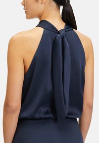 Granatowy top na halter z teksturowanej tkaniny. Posiada zawiązanie z tyłu oraz odkryty krój pleców, zapewniając luźny fason.
