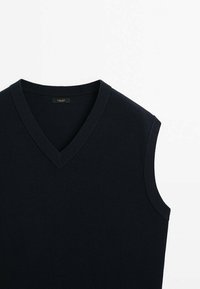 Pull sans manches bleu marine en maille, avec un décolleté en V, présentant une texture côtelée et des bords nets. Étiquette de logo discrète à l'intérieur du col.