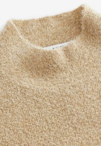 Beżowy sweter dzianinowy z wysokim, okrągłym dekoltem. Materiał charakteryzuje się miękką, puszystą teksturą i nieco luźnym splotem.