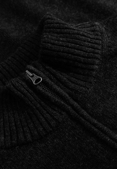 Pull en laine noir avec un col côtelé haut, présentant un détail zippé. Texture douce, gros plan montrant le tissage du tissu et les coutures.