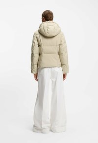 Beige pufferjakke med hætte, med vandret quiltning, elastiske manchetter og en let figursyet silhuet, kombineret med hvide culottebukser.