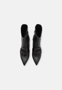 Bottines en cuir noir avec un bout pointu, dotées d'une sangle décorative et d'un détail de boucle. Texture lisse et design épuré.