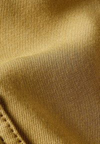 Tessuto testurizzato di un caldo colore senape, caratterizzato da un motivo intrecciato con una superficie morbida, che mostra una leggera lucentezza e dettagli di cucitura.