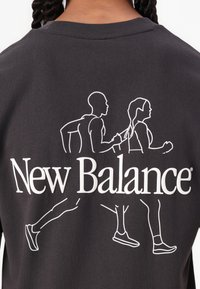 Dark gray T-shirt featuring a white outline graphic of two runners and the "New Balance" logo below in bold white letters.