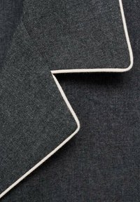 Tela de lana gris oscuro con bordes de pipa blanca, plegada para mostrar el detalle de contraste en un material de textura suave.