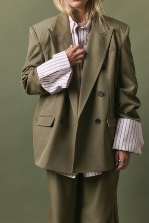 Õlivärvi üleõlgne bleiser topelt nuppudega, kombineeritud heleda roosa triibulise särgiga, millel on laiad mansetid. Sile kangas, mugav lõige.