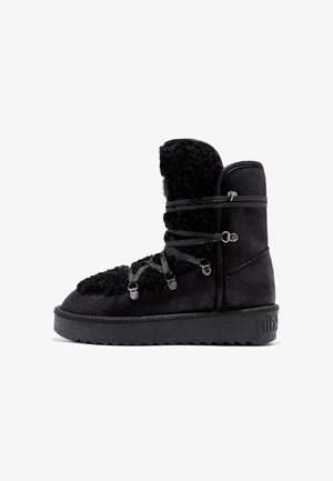 Botín negro hasta el tobillo hecho de gamuza y material suave, con cordones gruesos, acentos metálicos y una suela texturizada para mayor tracción.