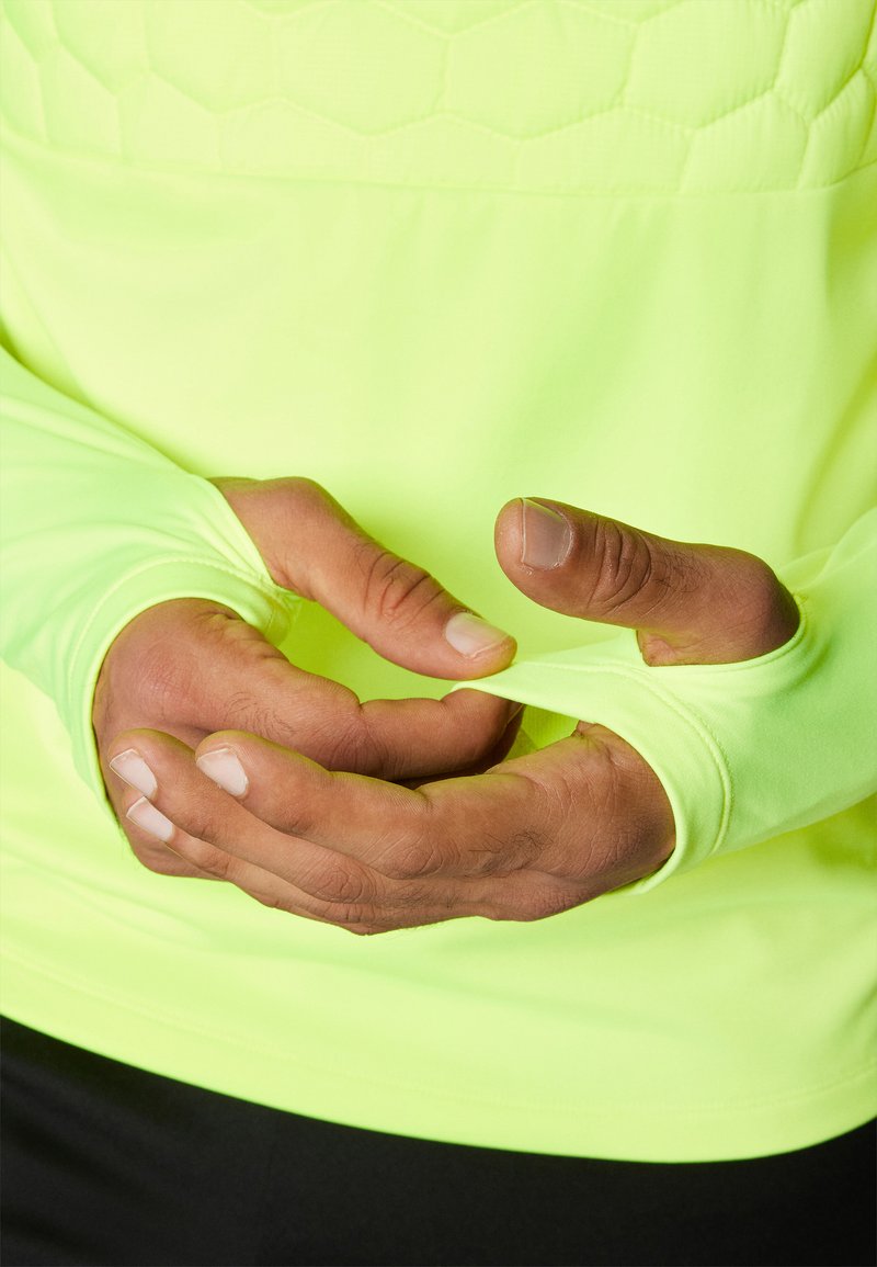 Maglietta sportiva a maniche lunghe di un vivace giallo neon, con un design testurizzato a esagoni sul petto e aperture per il pollice nelle maniche.