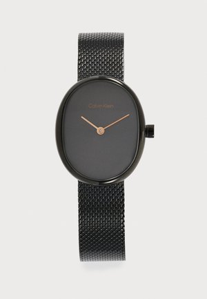 Schwarze ovale Calvin Klein Uhr mit schwarzem Mesh-Armband und minimal goldenen Stunden- und Minutenzeigern auf dunklem Zifferblatt.