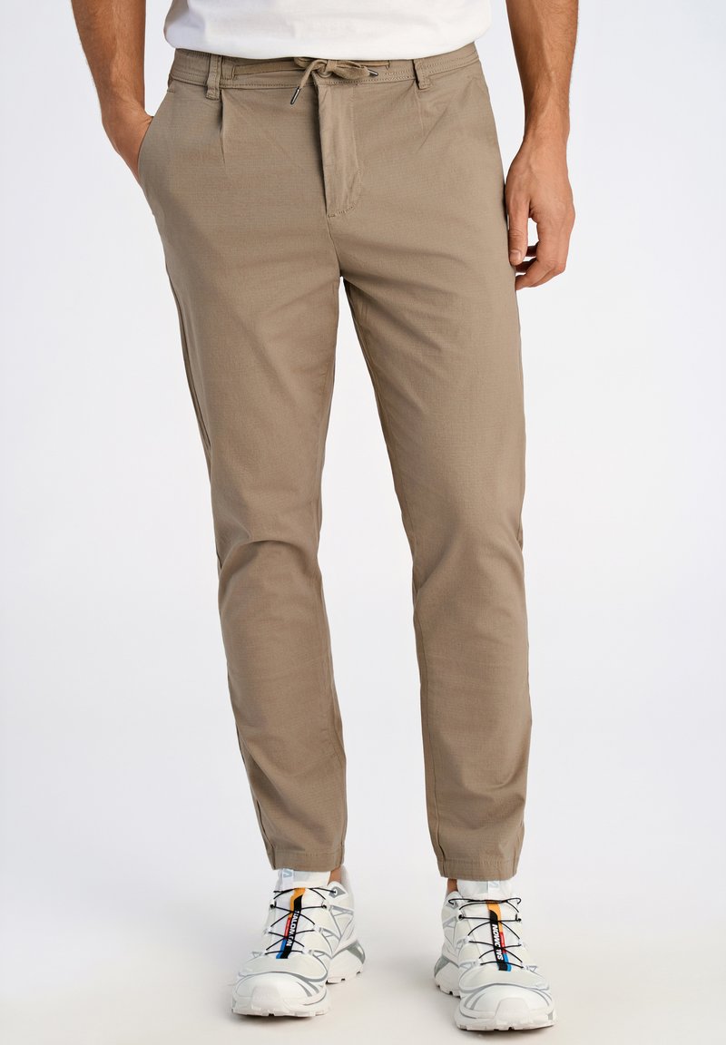 Beige broeken met een trekkoord in de taille, slim fit, gladde textuur en zijzakken, gecombineerd met witte sportschoenen met meerkleurige accenten.