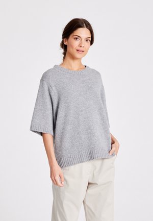 Vale vaaleanharmaa neulepusero, jossa on leveä kaula-aukko, lyhyet hihat ja ribattu helma, yhdistettynä beigeihin housuihin. Pehmeä rakenne ja rento muotoilu.