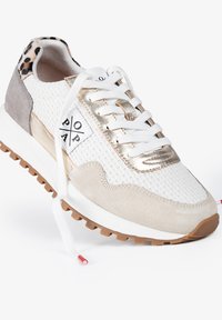 Las zapatillas de malla blancas presentan acentos dorados, paneles de ante beige y una suela de goma marrón texturizada. Incluyen cordones blancos y un detalle de estampado de leopardo en el talón.