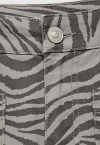 Grå denimtyg med ett svart zebramönster. Har en metallknapp med "KING DENIM COLLECTION" ingraverat. Strukturerad yta.