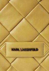 Yellow quilted leather surface with a stitched label displaying metallic "KARL LAGERFELD" branding in the center.