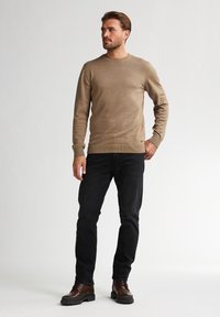 Maglione a maglia marrone con scollatura a girocollo, maniche lunghe e polsini a coste, abbinato a jeans neri e stivali marroni con lacci.