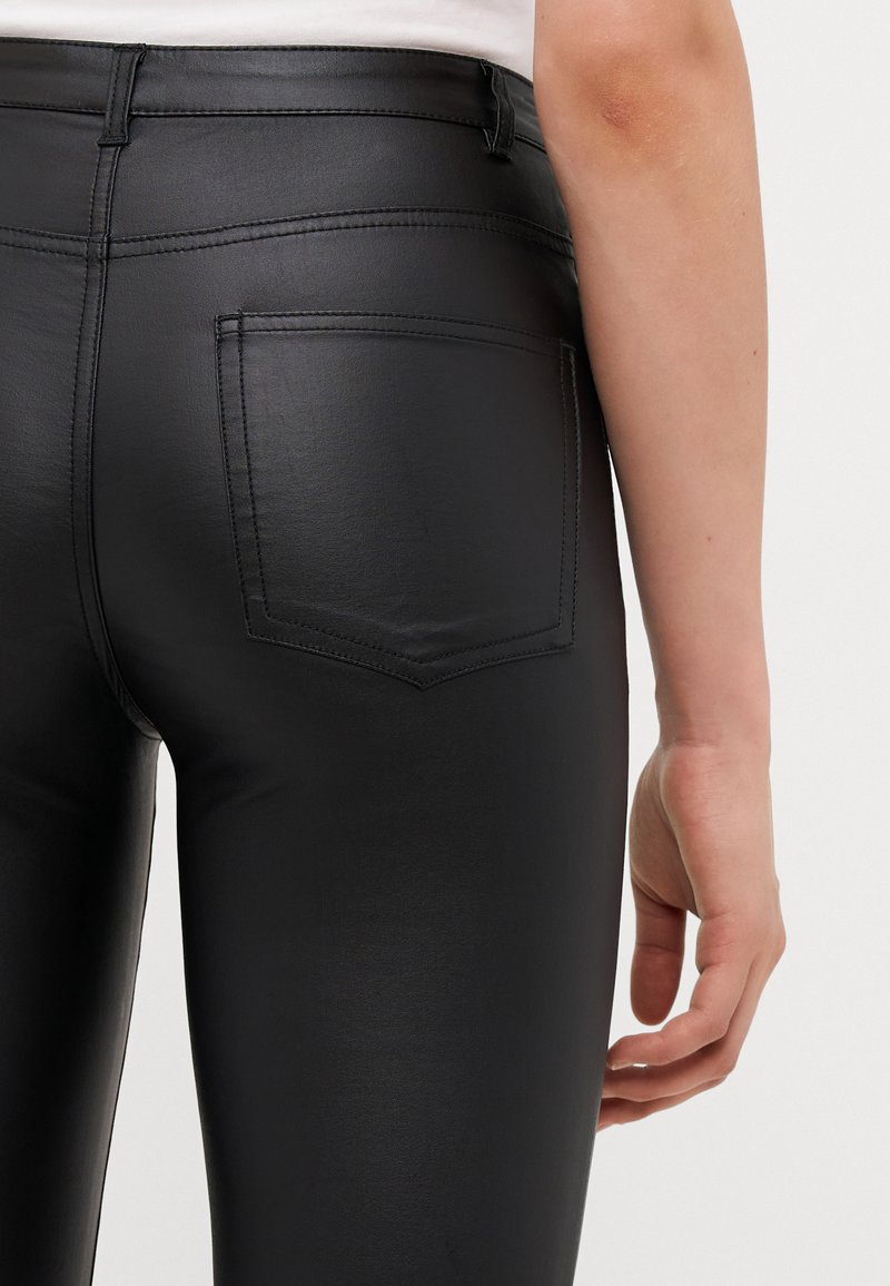 Schwarze Kunstlederhosen mit glatter Textur, hohem Bund und einer Gesäßtasche. Merkmale sichtbarer Nähte und einem figurbetonten Schnitt.