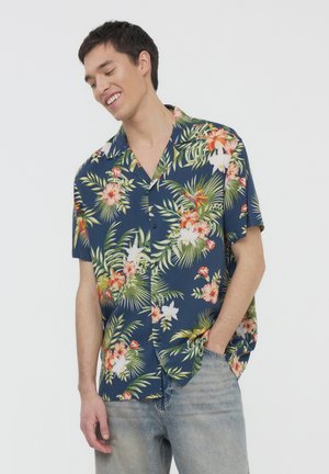 Camicetta a maniche corte di colore blu navy con motivo floreale tropicale, caratterizzata da foglie verdi e fiori vivaci. Vestibilità rilassata, tessuto leggero.