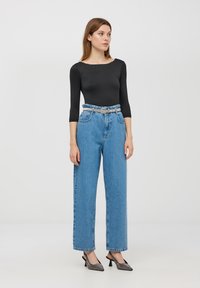 Czarna dopasowana bodysuit z długim rękawem, jasnoniebieskie dżinsy z wysokim stanem i paskiem oraz czarne szpilki z metalicznymi akcentami.