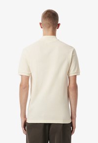 Beige polotröja tillverkad av mjukt tyg, med en klassisk krage och korta ärmar, med en ren, enkel design och inga synliga mönster.