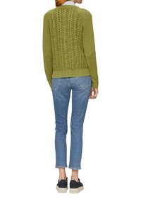 Zielony sweter z dzianiny z teksturowanym tyłem, w połączeniu z jasnoniebieskimi dżinsami oraz czarnymi butami z grubą, beżową podeszwą.