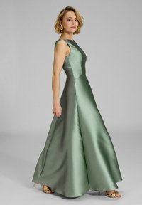 Abito da sera verde in satin con corpino aderente e gonna svasata. Presenta una texture liscia e un design senza maniche, accentuato da tacchi dorati.