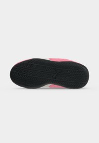 Semelle en caoutchouc noire texturée d'une sneaker rose et blanche avec le logo de la marque au centre, présentée sur un fond blanc uni.