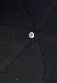Casquette en tissu noir avec un design cousu et un bouton logo métallique. La texture est lisse avec des coutures et des accents visibles.