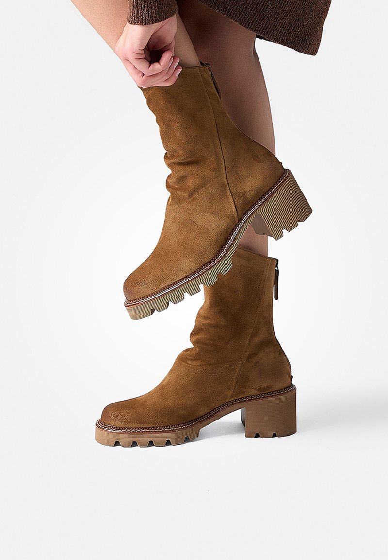 Bottines en daim marron avec un design décontracté, semelles à motif chunky et fermeture éclair sur le côté. Présentent un épais talon carré et des accents cousus.
