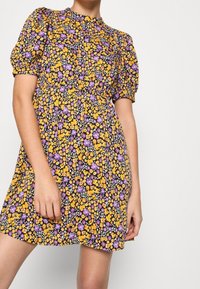 Blommig klänning med svart bakgrund och gula samt lila blommor, korta puffärmar och insydd midja, i ett lätt tyg.