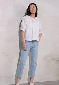 Blusa branca de mangas bufantes com decote redondo, combinada com jeans de perna reta azul claro. O look é completado com sapatos de salto brancos.