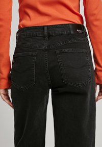 Svarta jeans med rak benmodell, hög midja, två bakfickor och en långärmad topp i orange med ribbade detaljer. Slät textur.