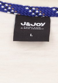 Etiket met "J&JOY," in witte tekst op een zwarte achtergrond. Geweven blauwe, witte en bruine accent aan de bovenkant. Maat "L." Gestructureerde stof achtergrond.