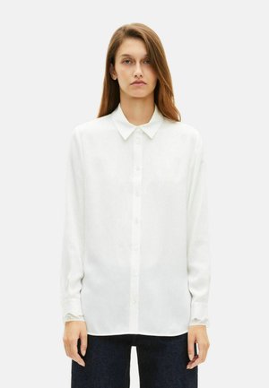 Blusa blanca de manga larga con cuello, cierre de botones en el frente y detalles de encaje en los puños, hecha de una tela suave y liviana.