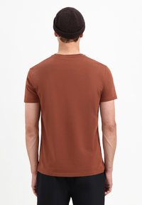 Bruine T-shirt met korte mouwen en een ronde halslijn, gemaakt van gladde stof. Gedragen met een donker gebreide muts, gezien vanuit de achterkant.