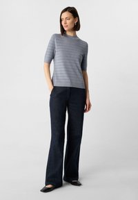 Helles blaues gestricktes Oberteil mit kurzen Ärmeln und einem Muster aus horizontalen Streifen, kombiniert mit dunkelblauen Schlaghosen und schwarzen flachen Schuhen.