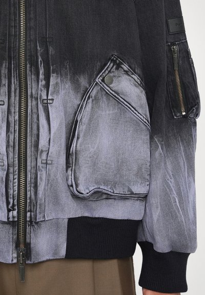Denim bomber jacket with a gradient black to gray fade, featuring multiple pockets, a ribbed hem, and silver hardware accents.