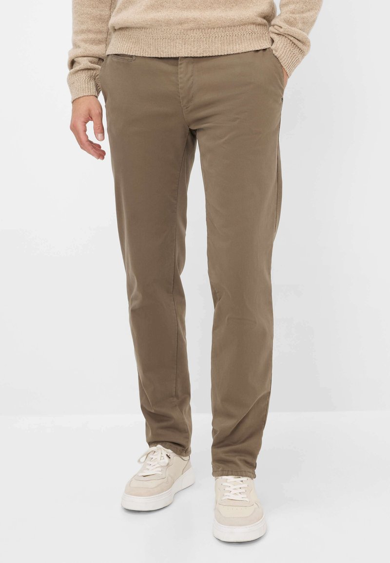 Maglione di lana beige sopra pantaloni marroni leggeri e aderenti. I pantaloni hanno tasche laterali e una texture liscia. Le sneaker sono beige con accenti bianchi.